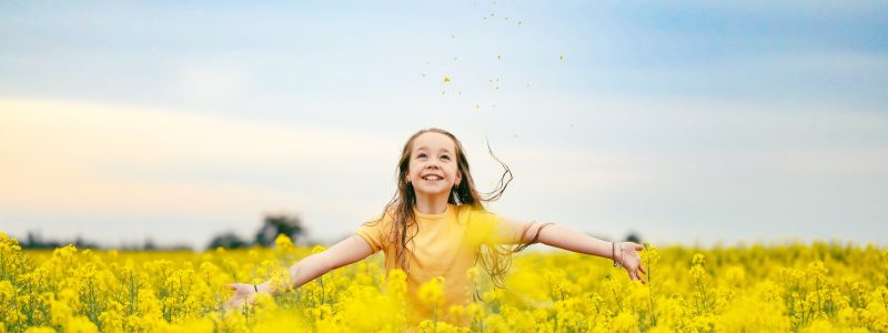 Pretty long haired girl playing in vibrant canola field in full bloom during Spring season